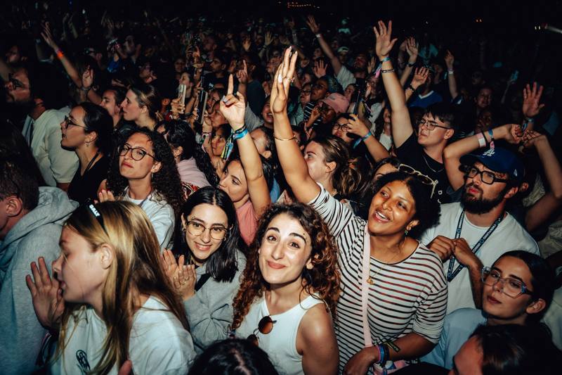 Festival-goers singing with hands raised in the crowd at night